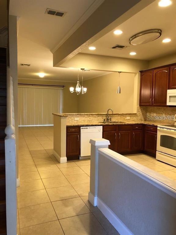 A kitchen with dark wood cabinets, tile flooring, and a breakfast bar overlooks a living area — 2850 POLVADERO LANE UNIT 105, ORLANDO, FL