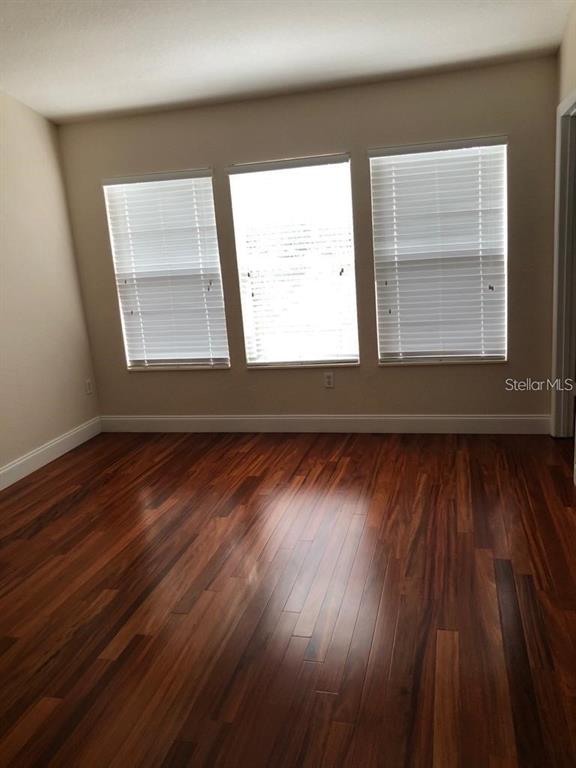 An empty room with dark hardwood floors and three windows featuring white horizontal blinds — 2850 POLVADERO LANE UNIT 105, ORLANDO, FL