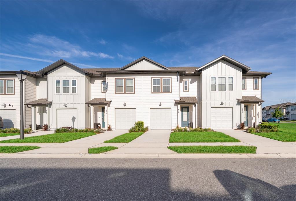 A row of white two-story townhomes with attached garages and concrete driveways under a blue sky — 634 LONGBOAT DRIVE, DAVENPORT, FL