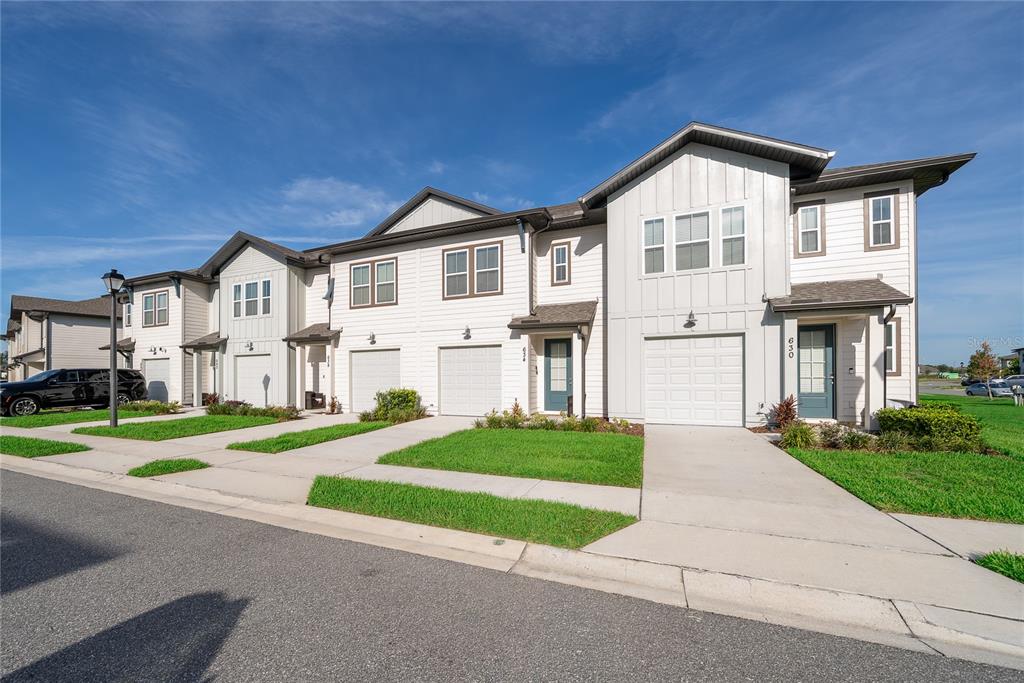 A row of modern two-story townhomes with white siding, attached garages, and concrete driveways — 634 LONGBOAT DRIVE, DAVENPORT, FL
