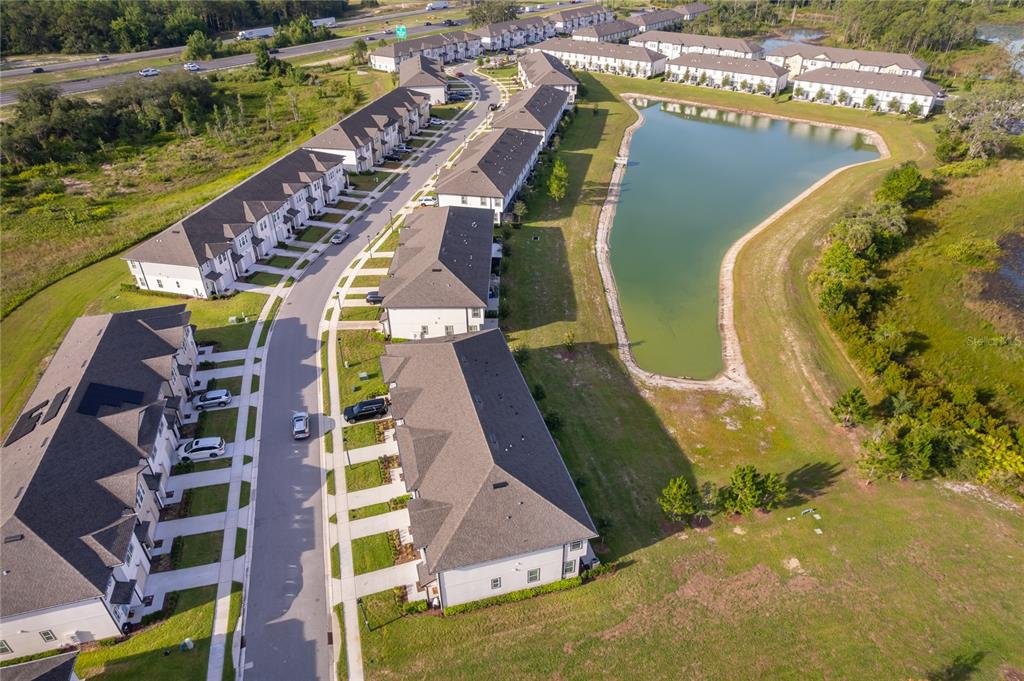 An aerial view shows a residential community with townhomes, a pond, and a nearby highway — 634 LONGBOAT DRIVE, DAVENPORT, FL