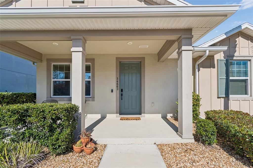 The exterior of a house features a covered front porch with a blue entry door — 14663 PROMENADE PARKWAY, ODESSA, FL