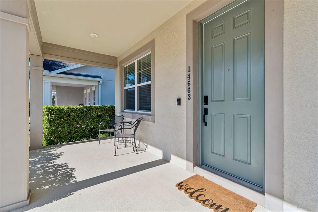 A covered front porch features a light blue door, two metal chairs, and a welcome mat — 14663 PROMENADE PARKWAY, ODESSA, FL