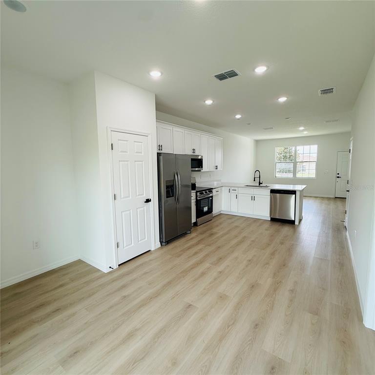A modern kitchen features white cabinetry, stainless steel appliances, and light wood-look flooring — 602 DESMOINES COURT, POINCIANA, FL