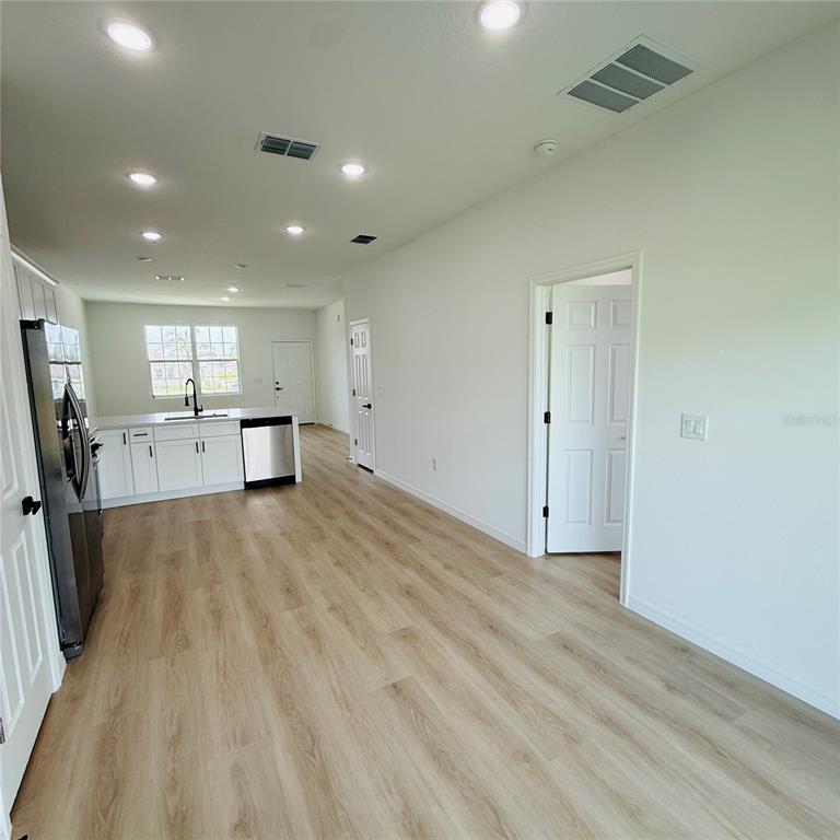 A kitchen with white cabinets and stainless steel appliances opens into a living area — 602 DESMOINES COURT, POINCIANA, FL