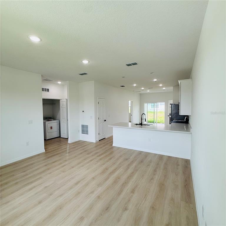 An open-concept living area features light wood-look flooring, recessed lighting, and a kitchen with white cabinets — 602 DESMOINES COURT, POINCIANA, FL