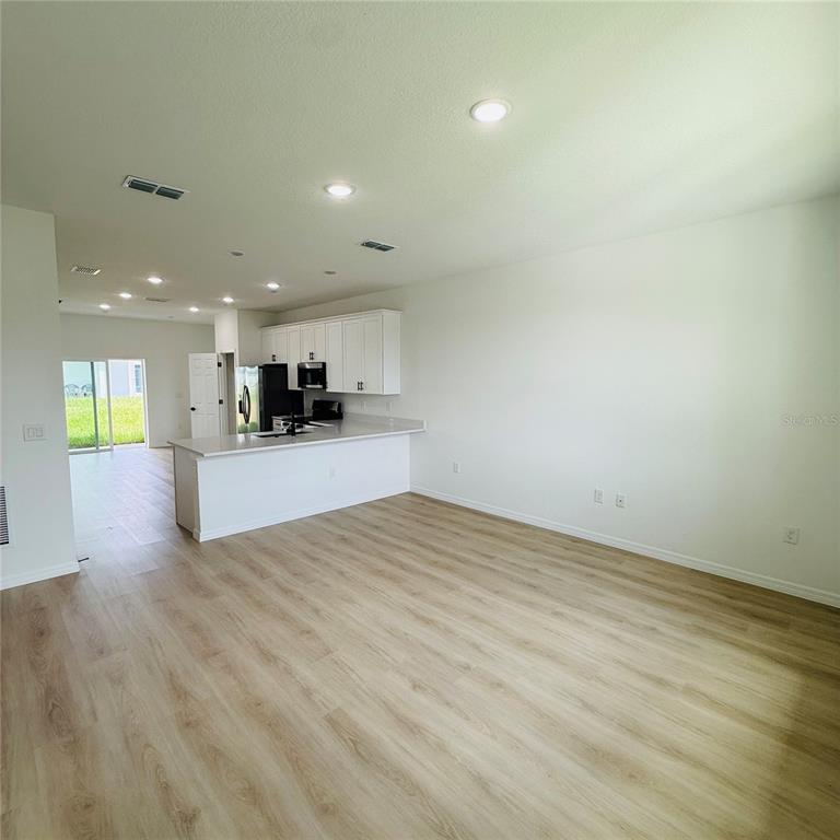 An open-concept kitchen with white cabinets and a breakfast bar overlooks a living area — 602 DESMOINES COURT, POINCIANA, FL