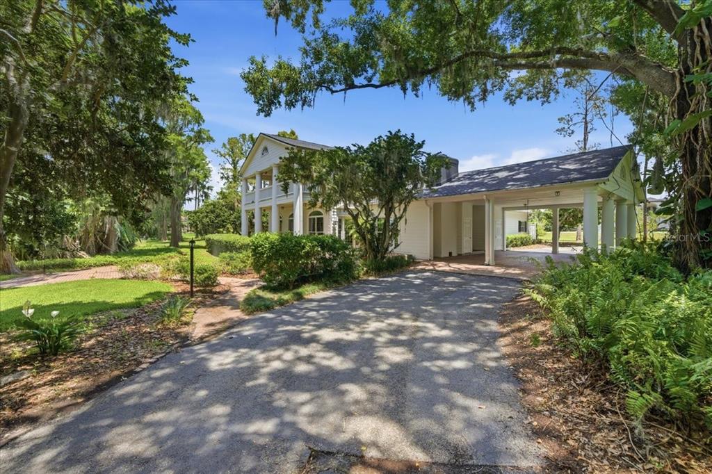 A two-story white house with a columned porch and an attached carport under large trees — 15612 HOWELL PARK LANE, TAMPA, FL