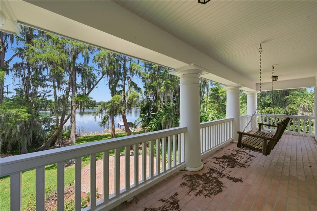 A covered porch with a hanging bench overlooks a lake surrounded by mossy trees — 15612 HOWELL PARK LANE, TAMPA, FL