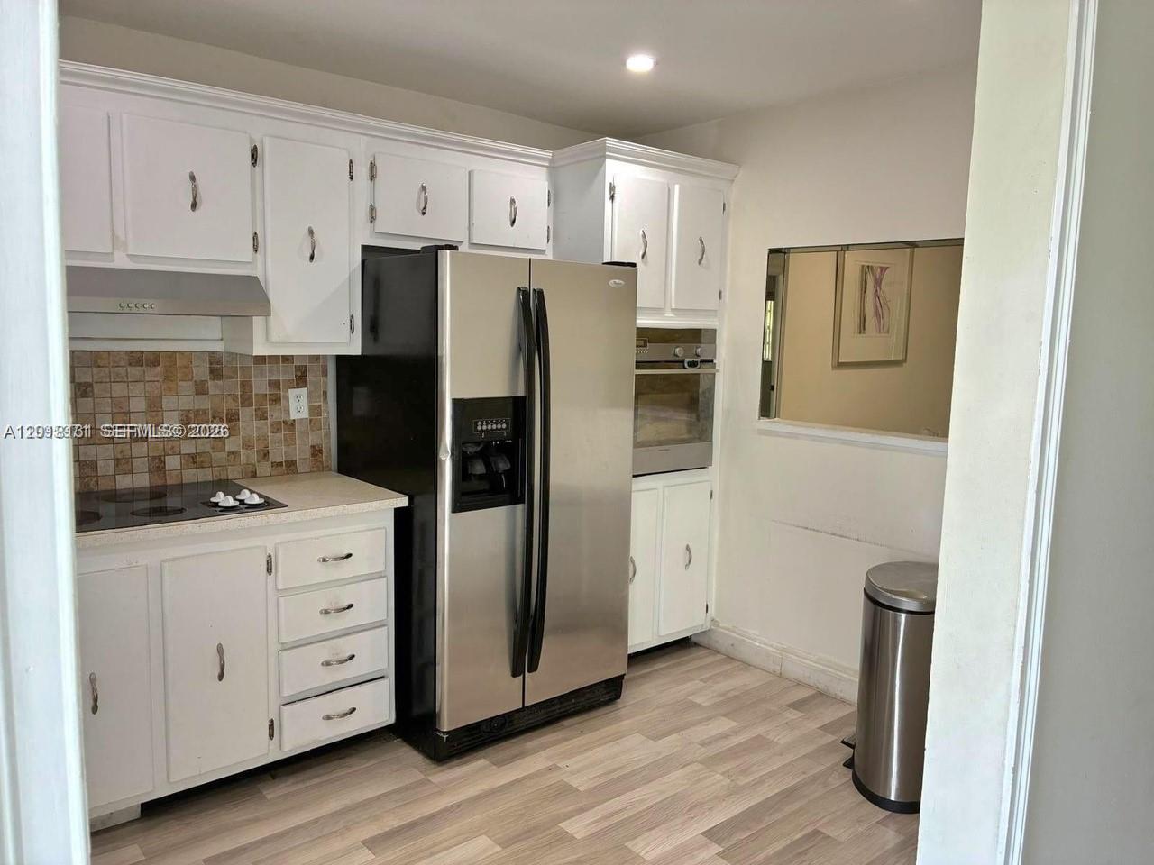 A kitchen features white cabinets, stainless steel appliances, a tiled backsplash, and wood-look flooring — 609 S State Road 7 # 2D, Margate FL 33068, MARGATE, FL