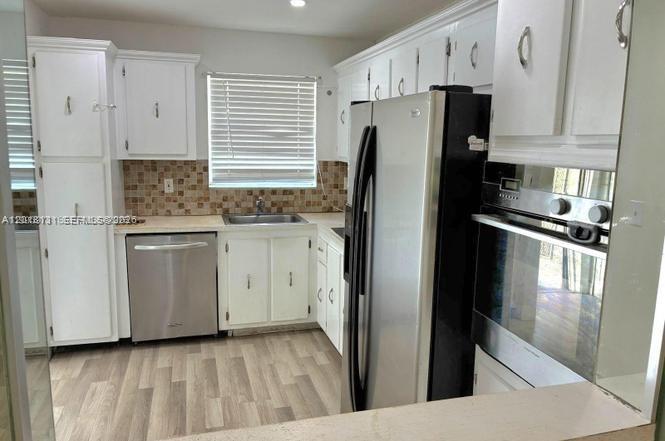 A kitchen features white cabinets, stainless steel appliances, a window with blinds, and wood-look flooring — 609 S State Road 7 # 2D, Margate FL 33068, MARGATE, FL