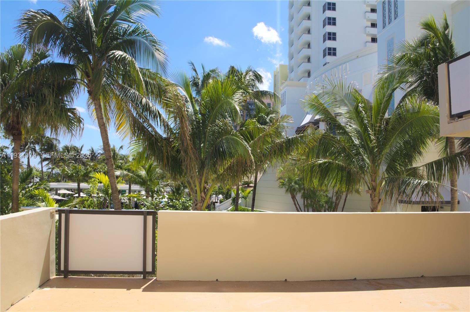 A balcony overlooks palm trees and a tall white building under a blue sky — 1623 Collins Ave # 218, Miami Beach FL 33139, MIAMI BEACH, FL