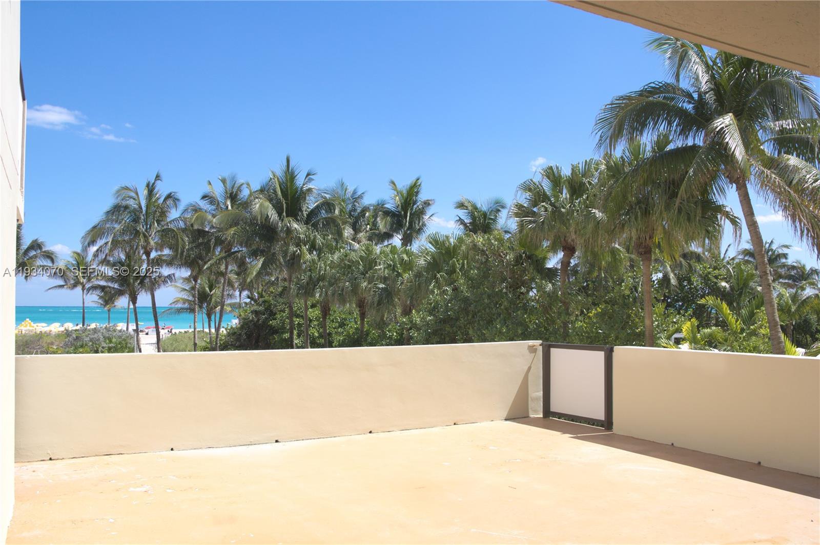 An outdoor balcony features a beige concrete floor, low walls, and a view of palm trees — 1623 Collins Ave # 218, Miami Beach FL 33139, MIAMI BEACH, FL