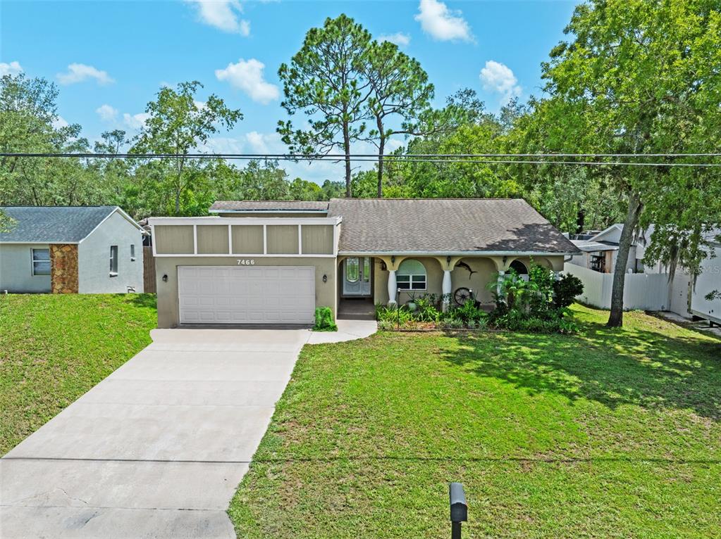 A single-story house with a two-car garage, a covered front porch, and a concrete driveway — 7466 APACHE TRAIL, SPRING HILL, FL