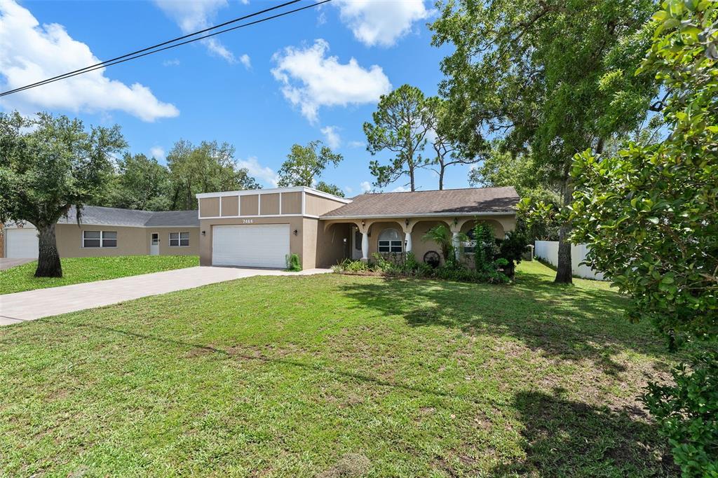 A single-story house with a tan exterior, a two-car garage, and an arched front porch — 7466 APACHE TRAIL, SPRING HILL, FL