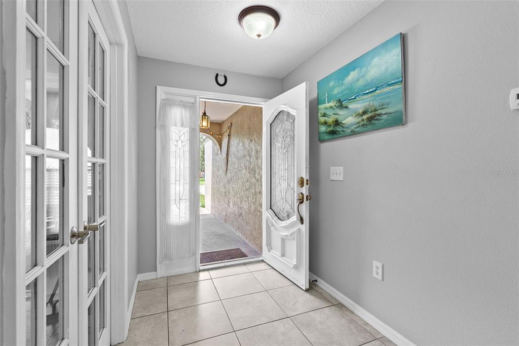 An entryway with light tile flooring, a white front door, and a coastal wall painting — 7466 APACHE TRAIL, SPRING HILL, FL