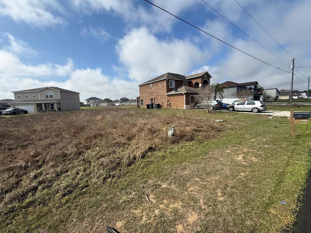 A vacant, grassy lot sits in front of two-story suburban houses under a cloudy sky — 2173 ROCK DRIVE, KISSIMMEE, FL