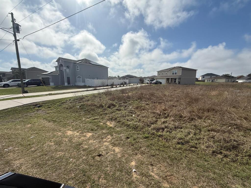 A vacant, grassy residential lot sits between two two-story houses under a cloudy sky — 2173 ROCK DRIVE, KISSIMMEE, FL