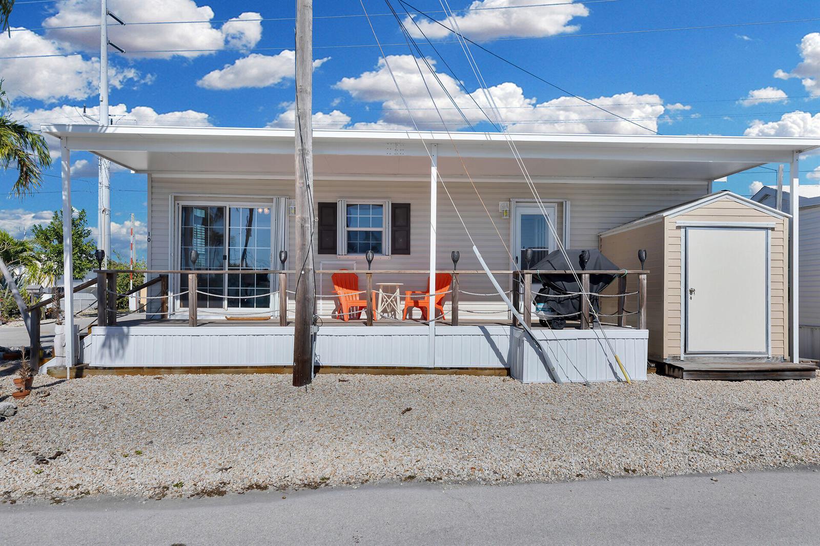 A single-story mobile home features a covered front deck with orange chairs and a shed — 1361 Overseas Highway, Marathon FL 33050, MARATHON, FL