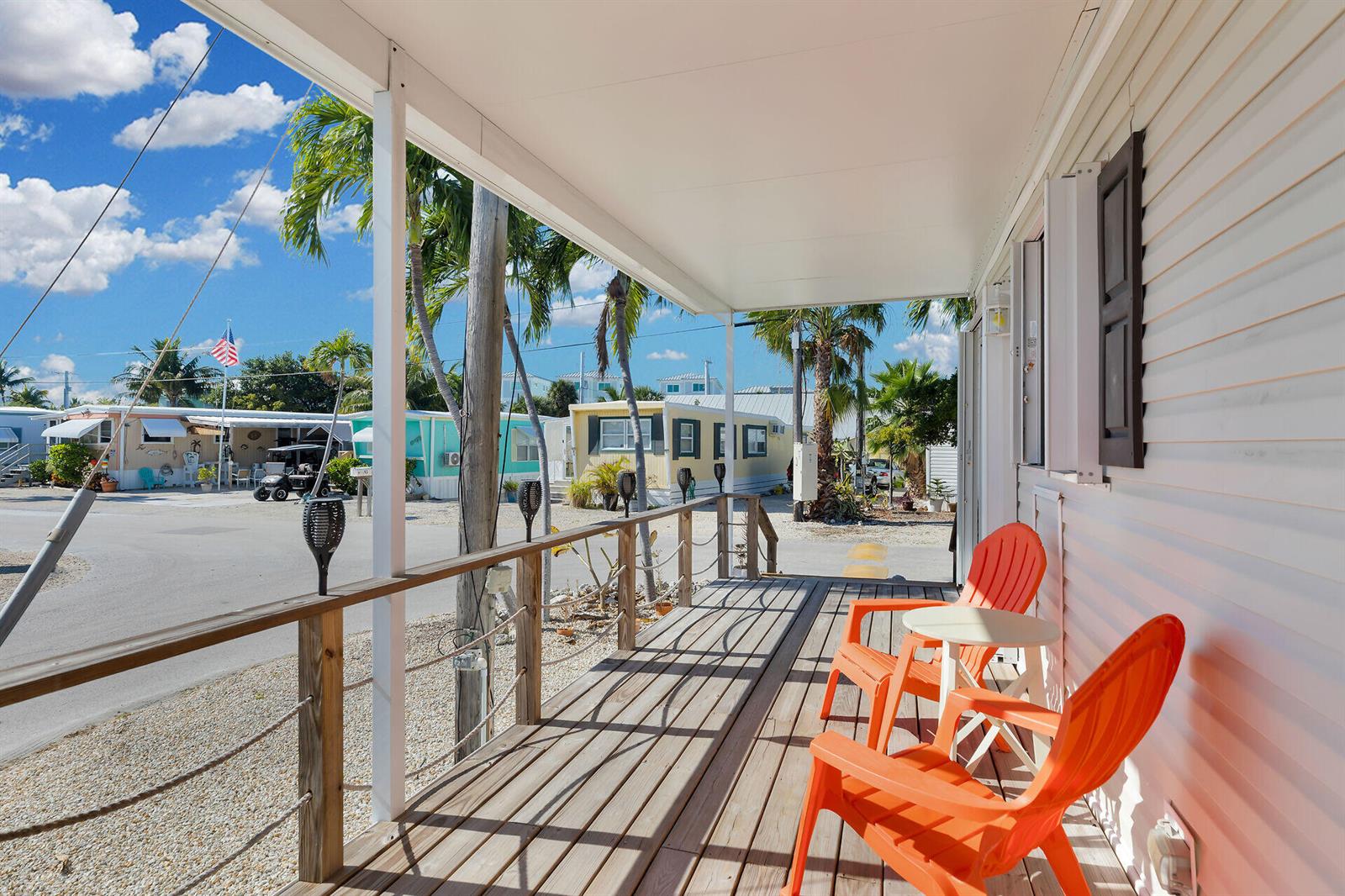 A covered wooden porch features two orange chairs and a small table overlooking a street — 1361 Overseas Highway, Marathon FL 33050, MARATHON, FL
