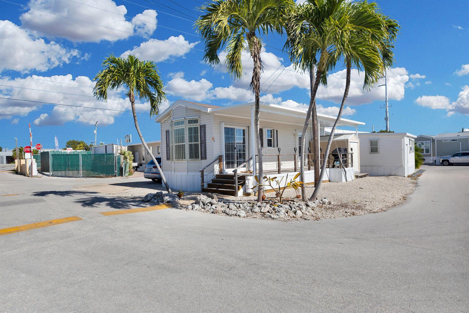 A single-story mobile home with a front porch and palm trees sits on a gravel lot — 1361 Overseas Highway, Marathon FL 33050, MARATHON, FL