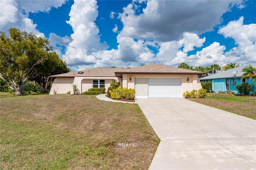 A single-story house with a beige exterior, a white garage door, and a concrete driveway — 26028 NORTHERN CROSS ROAD, PUNTA GORDA, FL