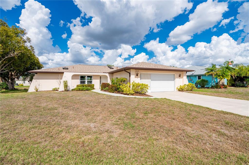 A single-story house with a tan exterior, a white garage door, and a grassy yard — 26028 NORTHERN CROSS ROAD, PUNTA GORDA, FL