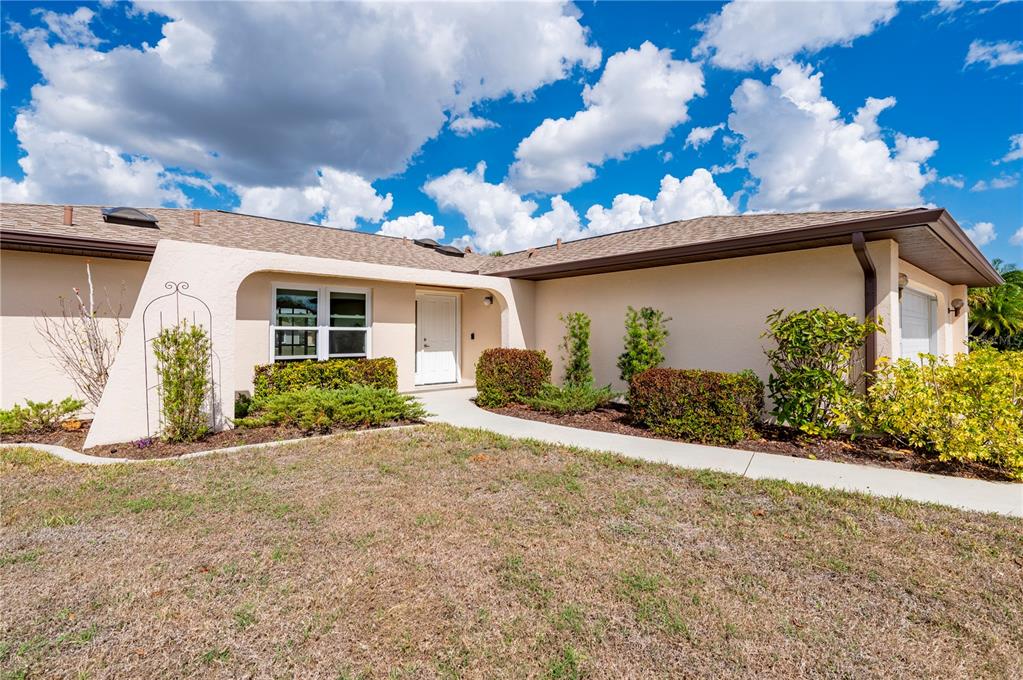 A single-story house with a tan stucco exterior, a white front door, and landscaped shrubs — 26028 NORTHERN CROSS ROAD, PUNTA GORDA, FL