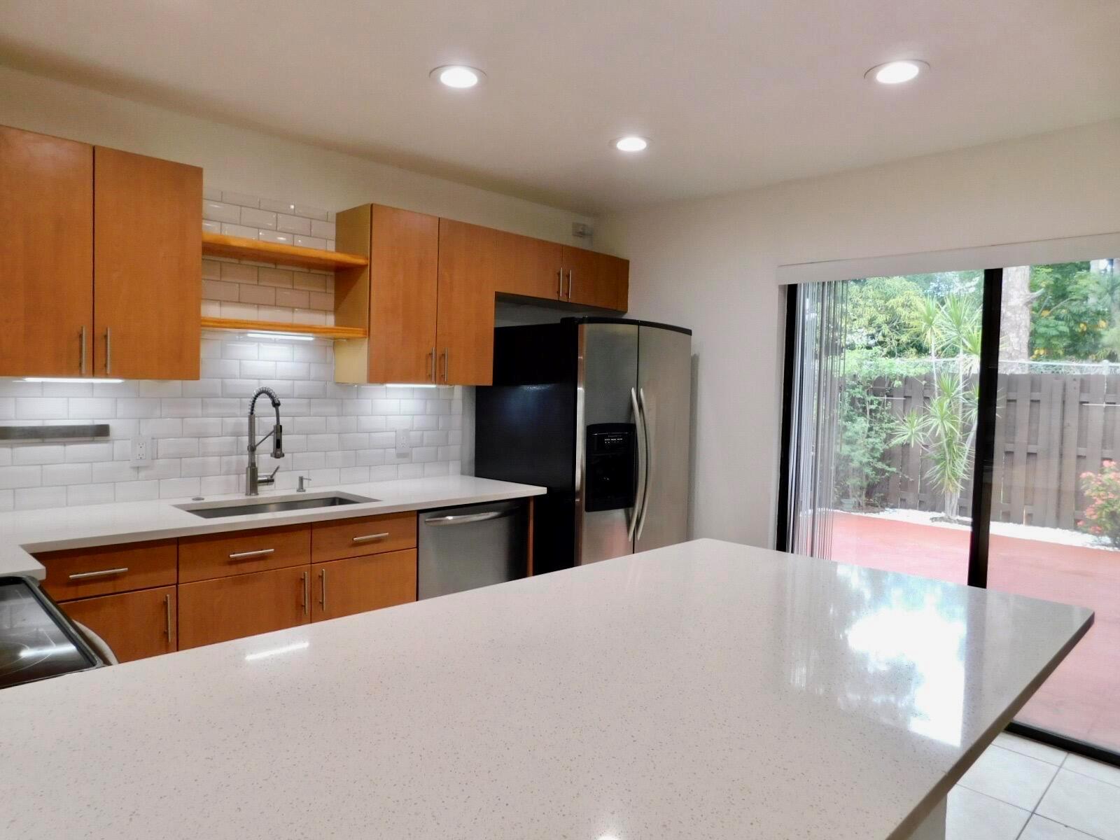 A modern kitchen features light wood cabinets, white quartz countertops, subway tile backsplash, and sliding doors — 4155 Turnberry Circle # 29, Lake Worth FL 33467, LAKE WORTH, FL