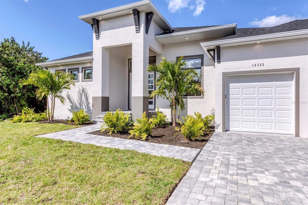 A modern single-story house exterior features white stucco walls, a paved driveway, and palm trees — 10209 COCOA BEACH STREET, PORT CHARLOTTE, FL