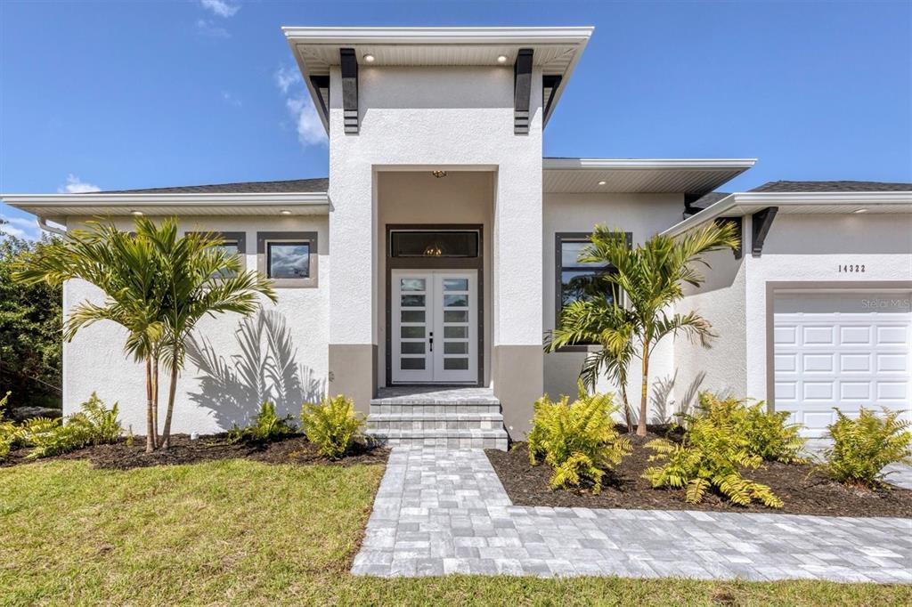 A modern single-story house exterior features a white stucco facade, double front doors, and palm trees — 10209 COCOA BEACH STREET, PORT CHARLOTTE, FL