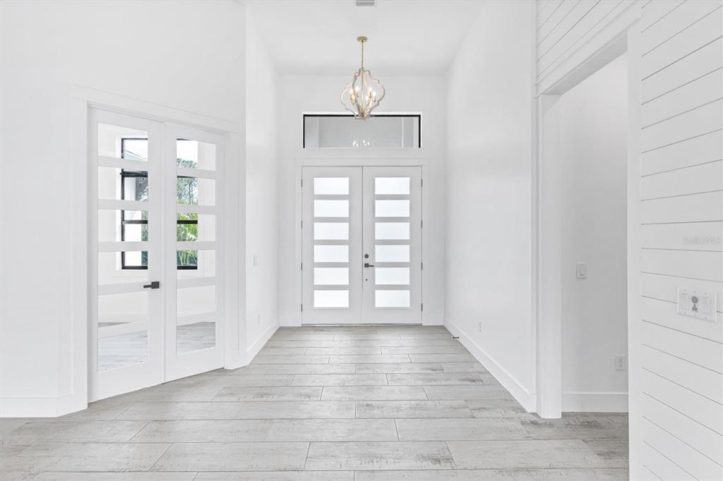 A bright entryway features white walls, light wood-look tile floors, and double glass-paneled doors — 10209 COCOA BEACH STREET, PORT CHARLOTTE, FL