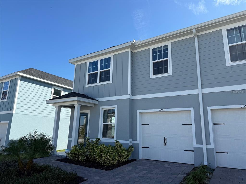A two-story townhouse with light blue siding, a white garage door, and a small porch — 1200 PORT BLUE WAY, LADY LAKE, FL