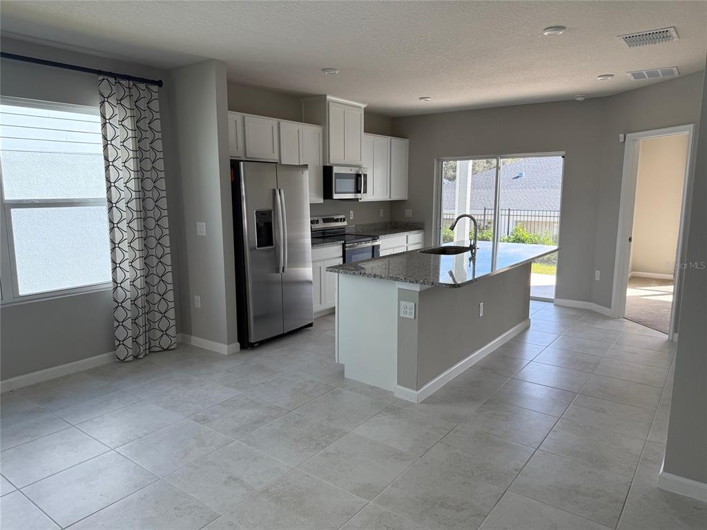 A kitchen features white cabinets, stainless steel appliances, a granite island, and light tile flooring — 1200 PORT BLUE WAY, LADY LAKE, FL