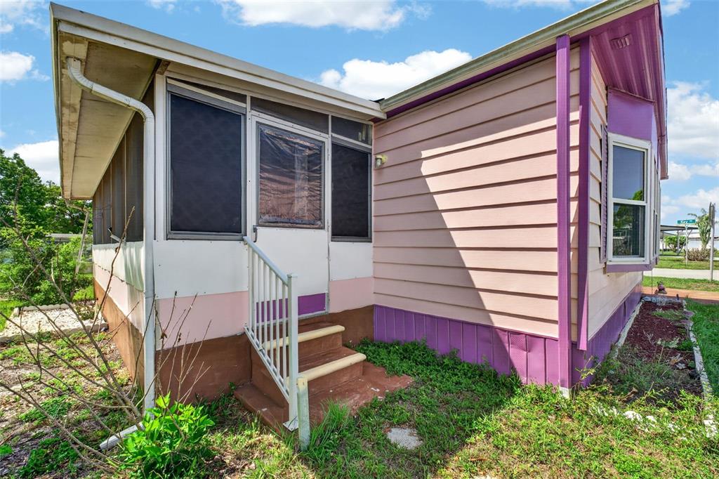 Exterior view of a mobile home with a screened porch, pink siding, and purple skirting — 2129 LOIS BOULEVARD, LAKE ALFRED, FL