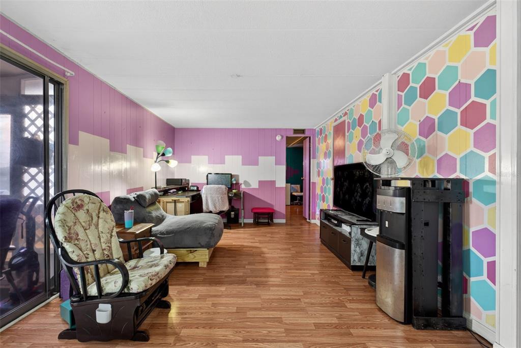 A living room features wood-look flooring, purple paneled walls, and a colorful hexagonal patterned accent wall — 2129 LOIS BOULEVARD, LAKE ALFRED, FL