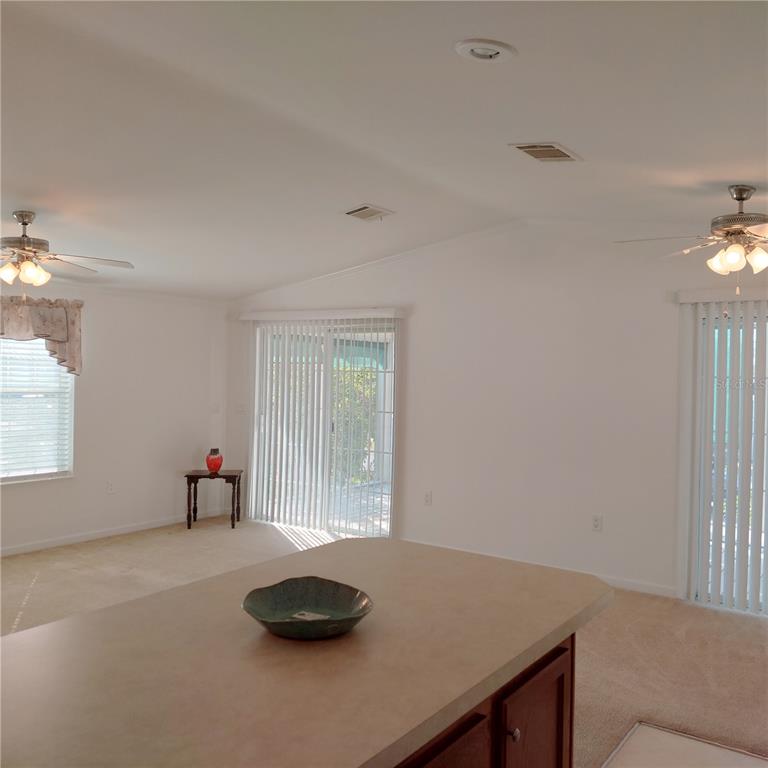 A kitchen island overlooks a living area with carpeted floors, ceiling fans, and sliding glass doors — 1760 DOROTHY BOULEVARD, LUTZ, FL