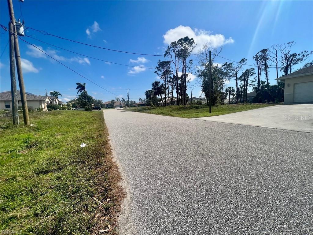 A paved street leads past a grassy lot toward houses under a blue sky — 5 PINE VALLEY COURT, ROTONDA WEST, FL