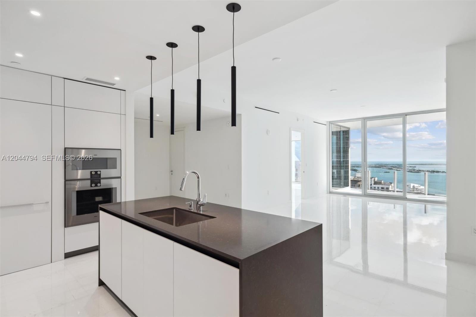 A modern kitchen features a dark countertop island, white cabinetry, and floor-to-ceiling windows with water views — 300 Biscayne Blvd Way # 3805W, Miami FL 33131, MIAMI, FL