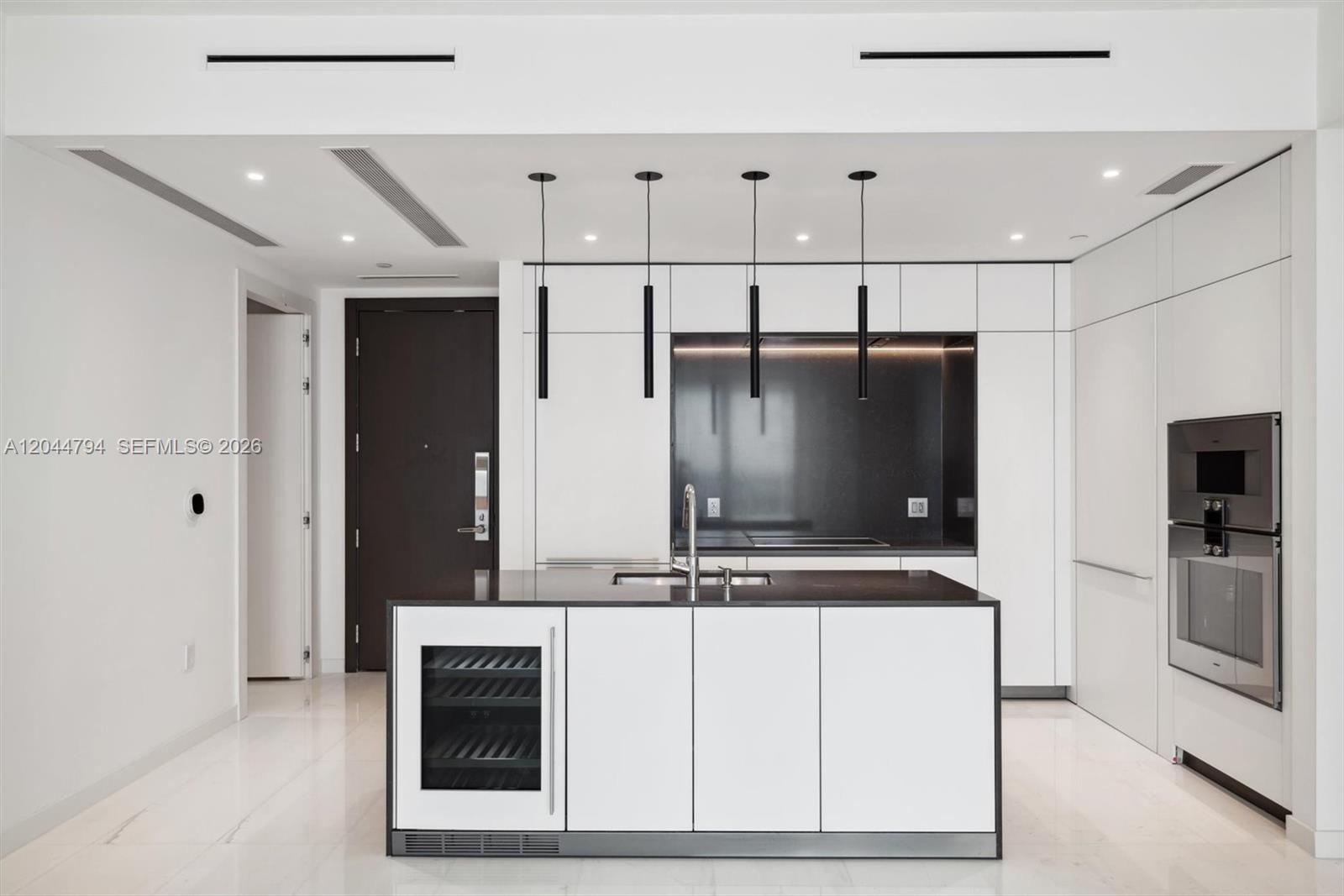 A modern kitchen features a white island with a wine cooler and dark countertops — 300 Biscayne Blvd Way # 3805W, Miami FL 33131, MIAMI, FL