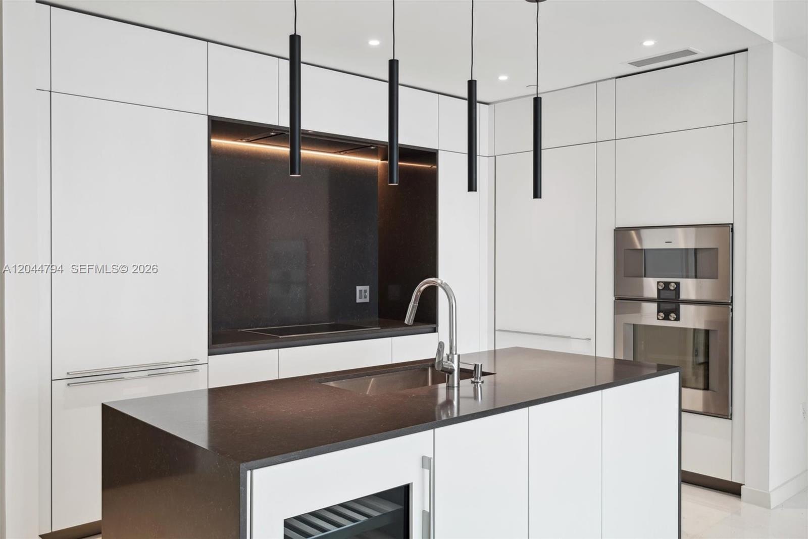 A modern kitchen features white cabinetry, a dark stone island with a sink, and pendant lighting — 300 Biscayne Blvd Way # 3805W, Miami FL 33131, MIAMI, FL