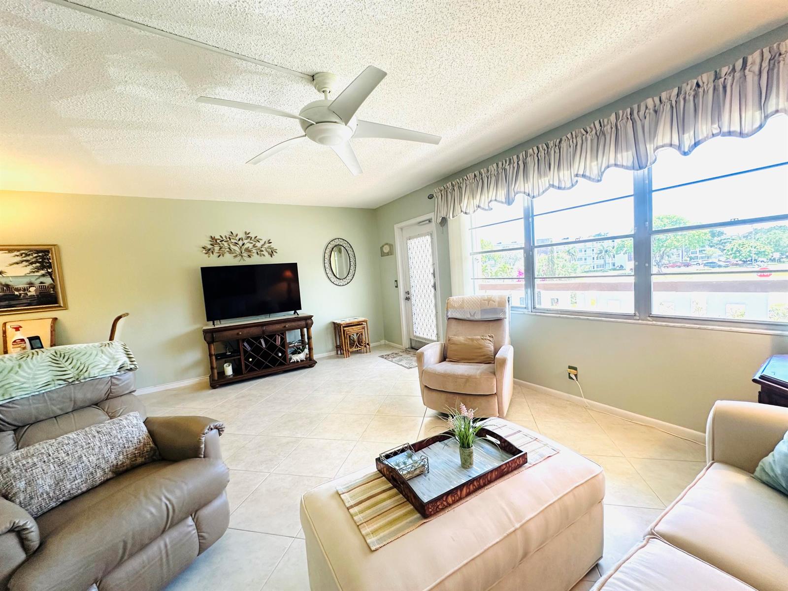 A living room features light green walls, tile flooring, a ceiling fan, and large windows — 2132 Cambridge F # 2132, Deerfield Beach FL 33442, DEERFIELD BEACH, FL
