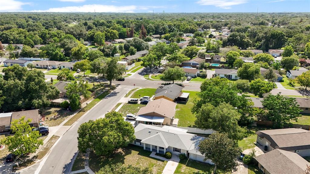 An aerial view shows a suburban neighborhood with single-family homes, tree-lined streets, and grassy yards — 142 BAYBERRY COURT, WINTER SPRINGS, FL