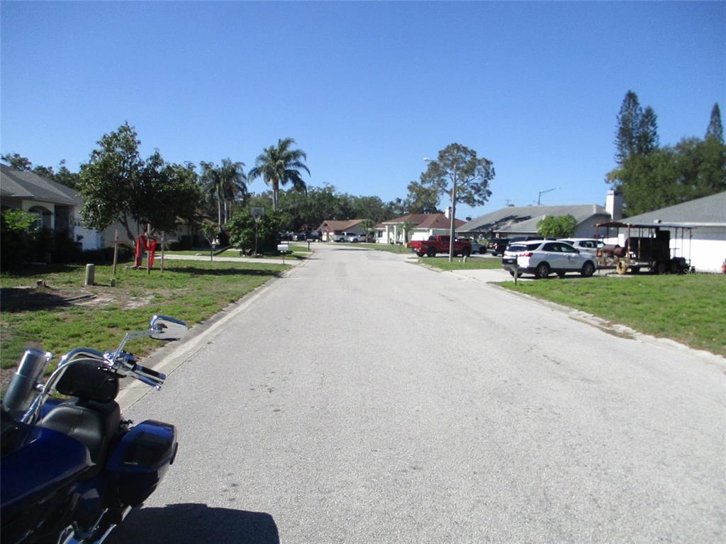 A view of a residential street with houses, parked vehicles, and a motorcycle in the foreground — 8904 PLANTERS LANE, NEW PORT RICHEY, FL