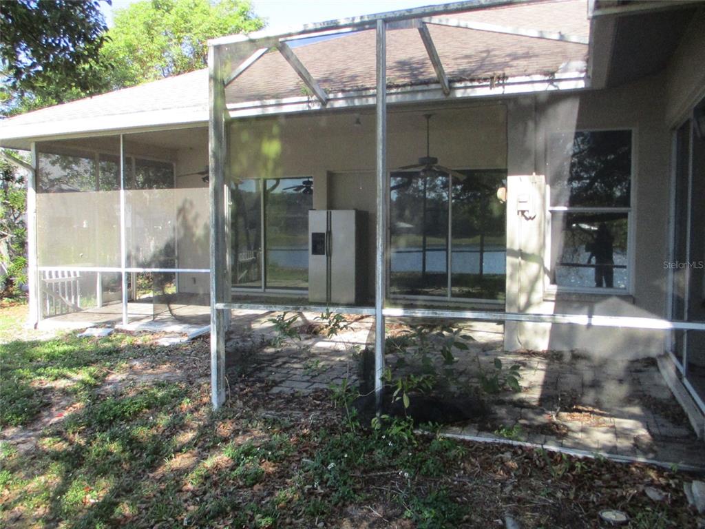 A screened-in patio features a paved floor, a refrigerator, and views of a lake — 8904 PLANTERS LANE, NEW PORT RICHEY, FL