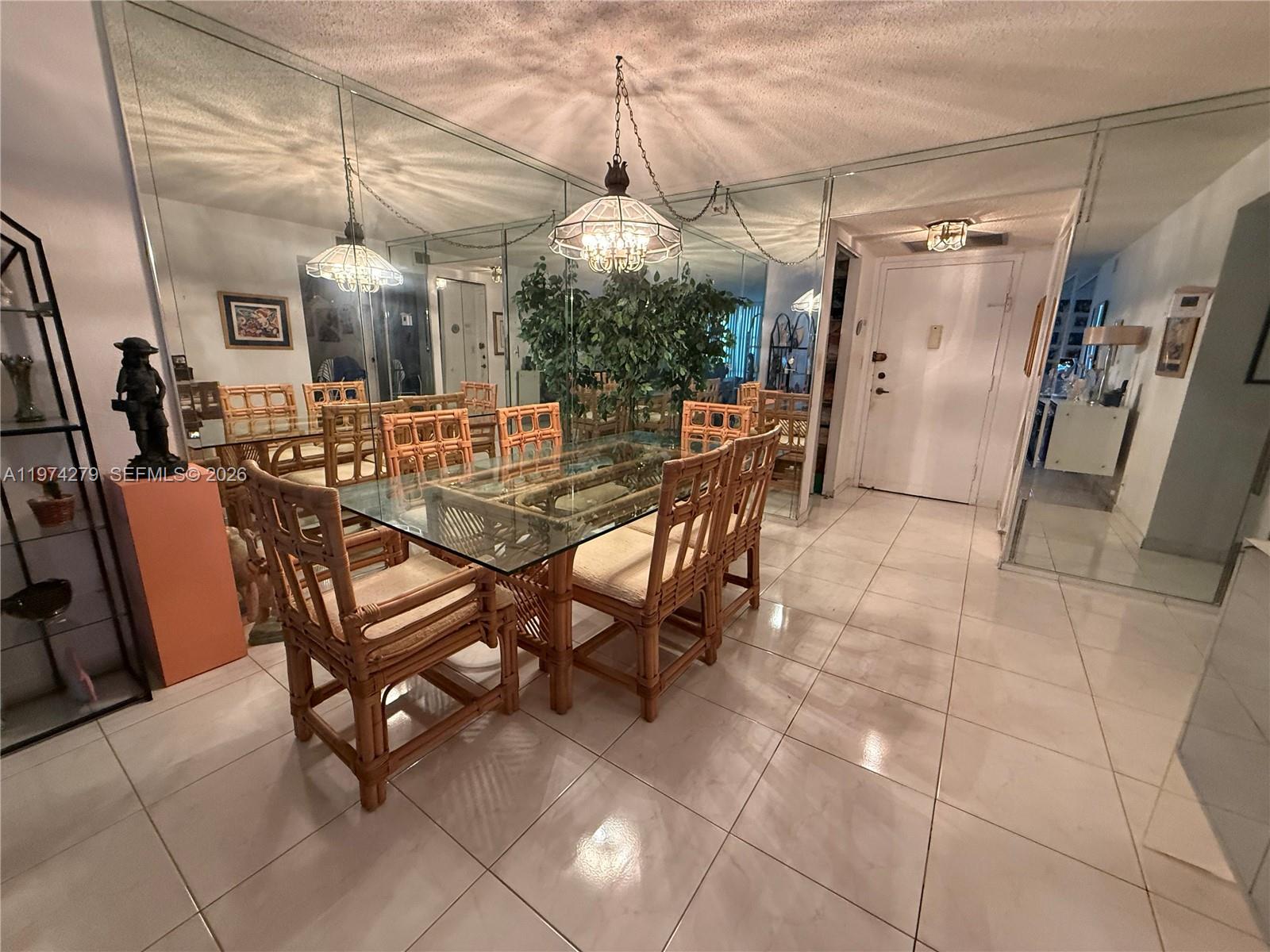 A dining room features a glass-topped rattan table, mirrored walls, and light-colored tile flooring — 1000 Parkview Dr # 1022, Hallandale Beach FL 33009, HALLANDALE BEACH, FL