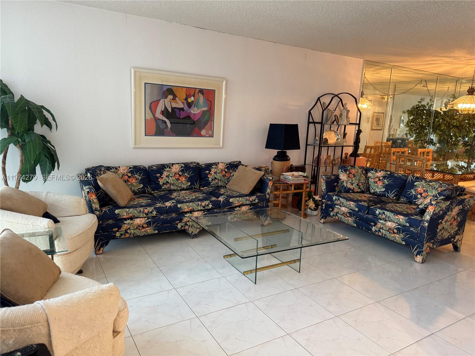 A living room features floral sofas, a glass coffee table, and white tiled flooring — 1000 Parkview Dr # 1022, Hallandale Beach FL 33009, HALLANDALE BEACH, FL