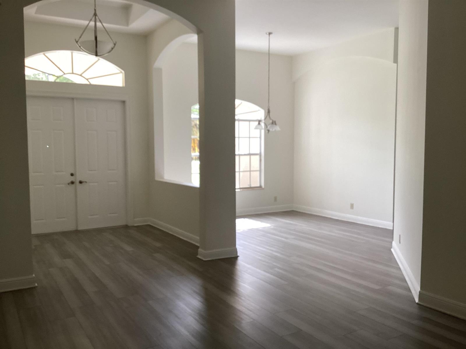 An entryway and adjacent dining area with white walls, arched openings, and grey wood flooring — 17119 Alexander Run, Jupiter FL 33478, JUPITER, FL