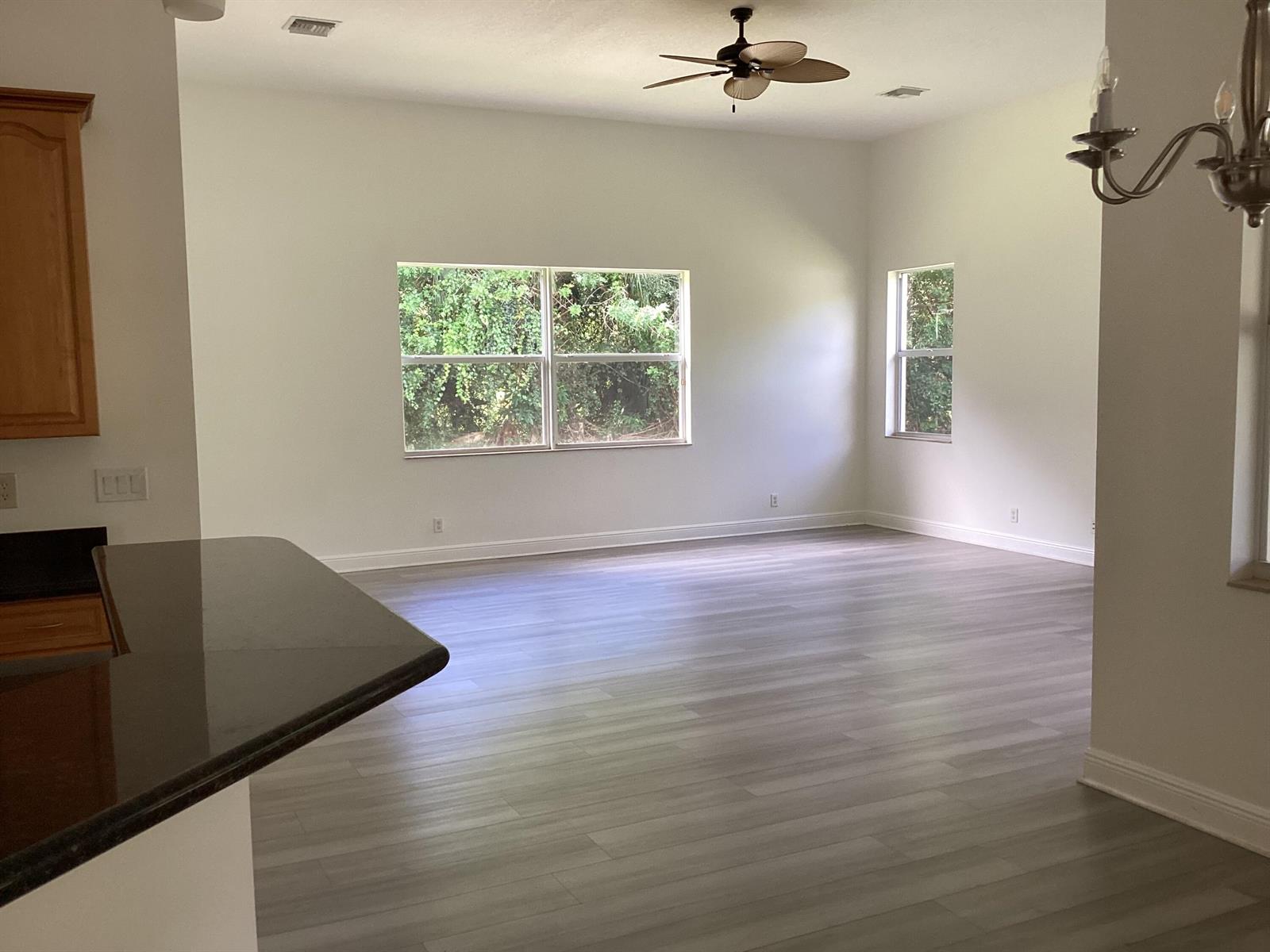 An open living area features light gray wood-look flooring, white walls, and a ceiling fan — 17119 Alexander Run, Jupiter FL 33478, JUPITER, FL