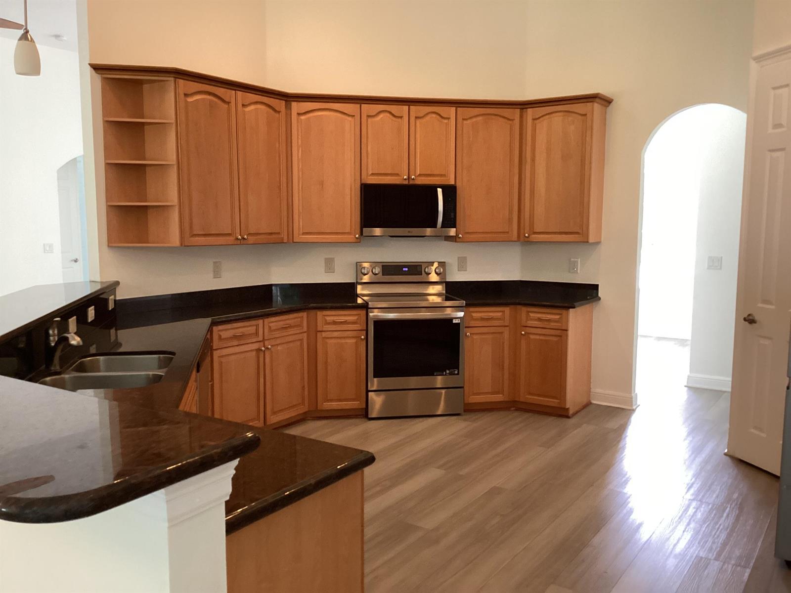 A kitchen features light wood cabinets, dark countertops, stainless steel appliances, and light-colored wood flooring — 17119 Alexander Run, Jupiter FL 33478, JUPITER, FL